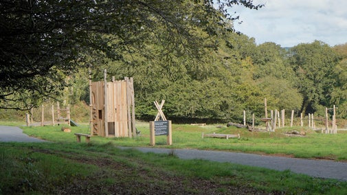 Looking out at play area which is lit by the sun in the distance and shows a tower made out of woods and logs to climb on